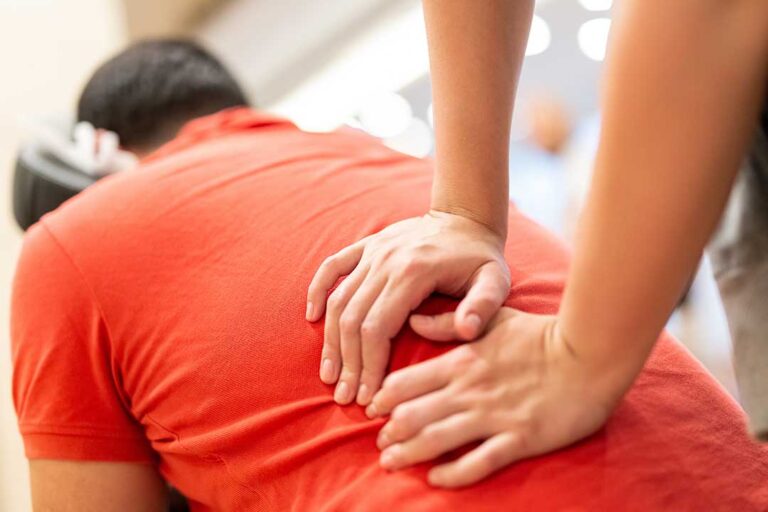 A clinician discusses back pain with an adult during a movement assessment in a bright treatment room.